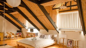 A bedroom with a sloped ceiling, wooden beams, a bed with pillows, a TV, and a bookshelf. - Sundowner Loft (Mossel Bay)