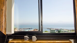 A view from a window overlooking a coastal area with a marina, boats, and distant mountains. - Sundowner Loft (Mossel Bay)