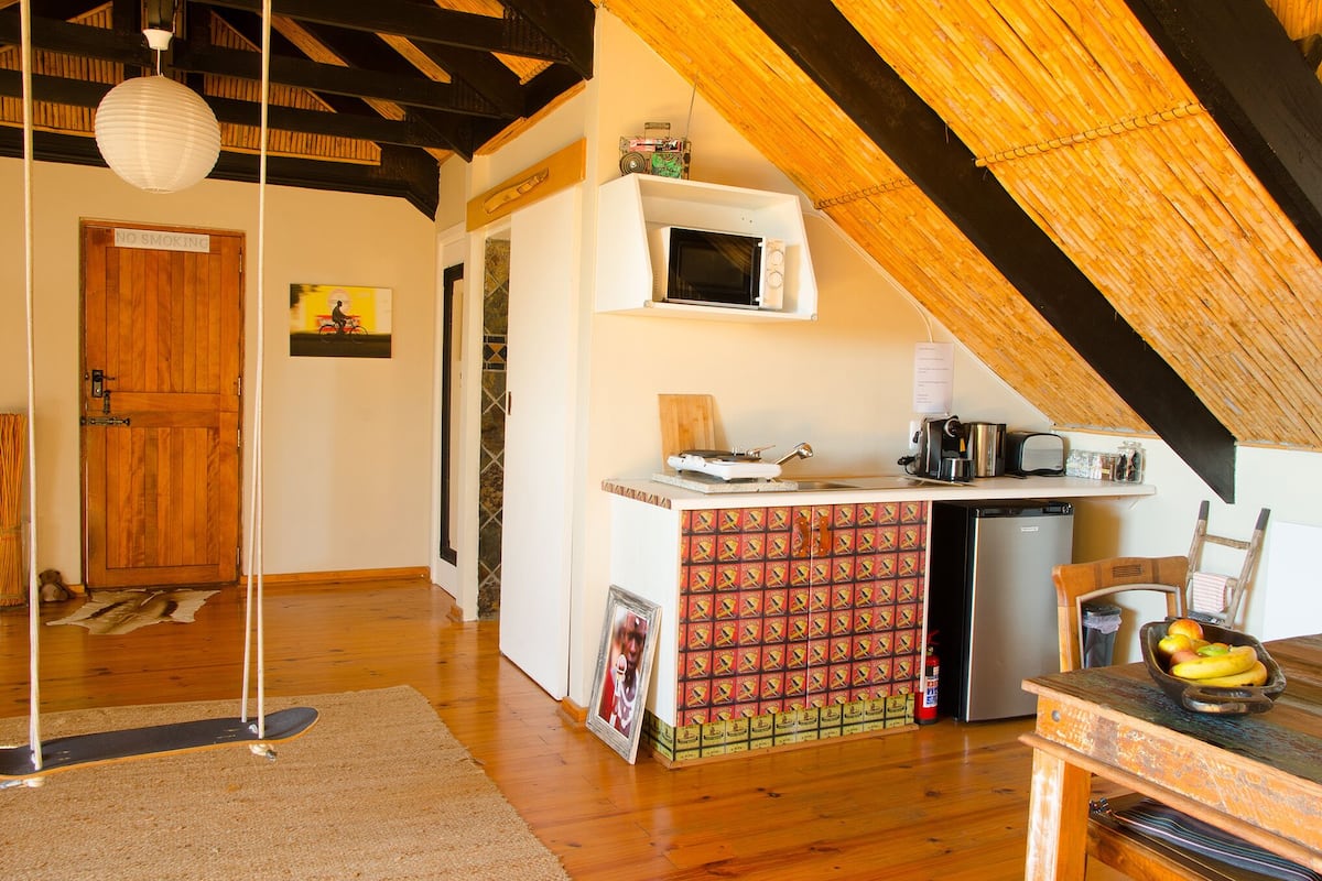 A kitchen with a microwave, a coffee maker, and a small refrigerator. There is a wooden door and a framed picture on the wall.