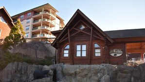Un chalet à l’extérieur rustique, avec un revêtement en bois, un mur en pierre orné d’une sculpture d’ours et une enseigne indiquant qu’il s’agit du Big Bear Lodge and Resort.
