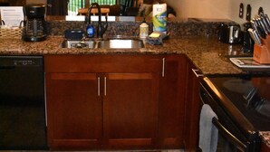 Une cuisine dotée de plans de travail en granit, de meubles en bois, d’un lave-vaisselle encastré, d’une cuisinière et d’une grande fenêtre offrant une vue dégagée.