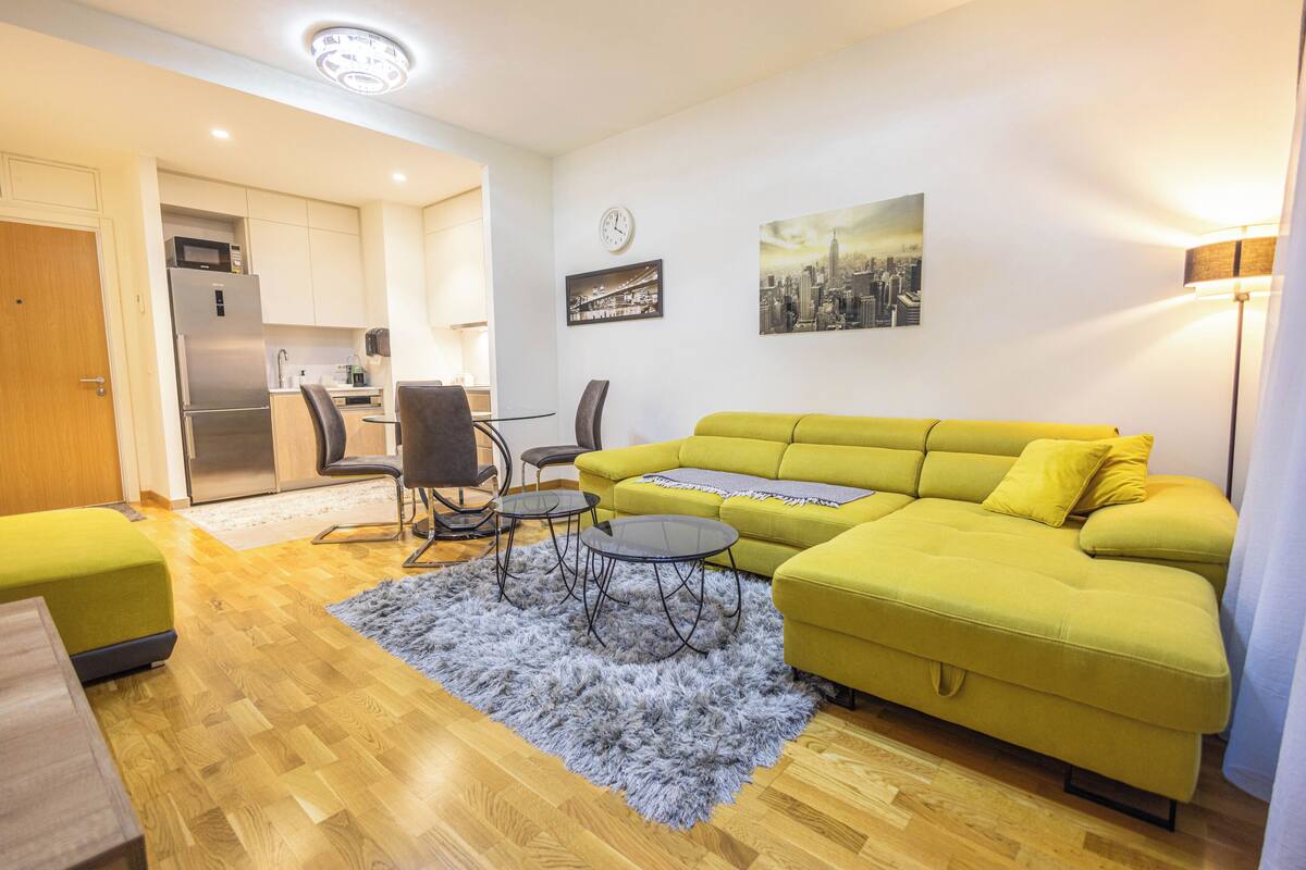A living room with a yellow sofa, a gray shag rug, and a dining area with a table and chairs.
