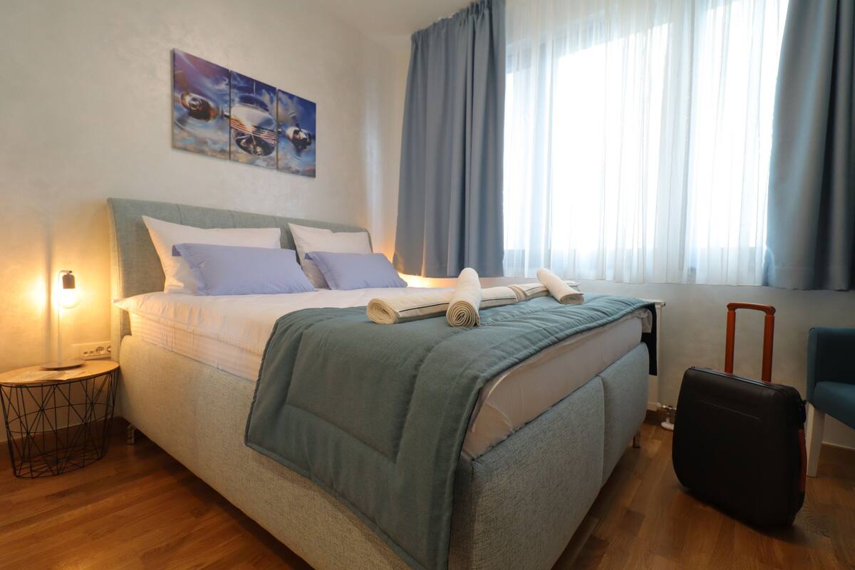 A neatly made bed with a blue blanket, a bedside lamp, and a suitcase on the floor.