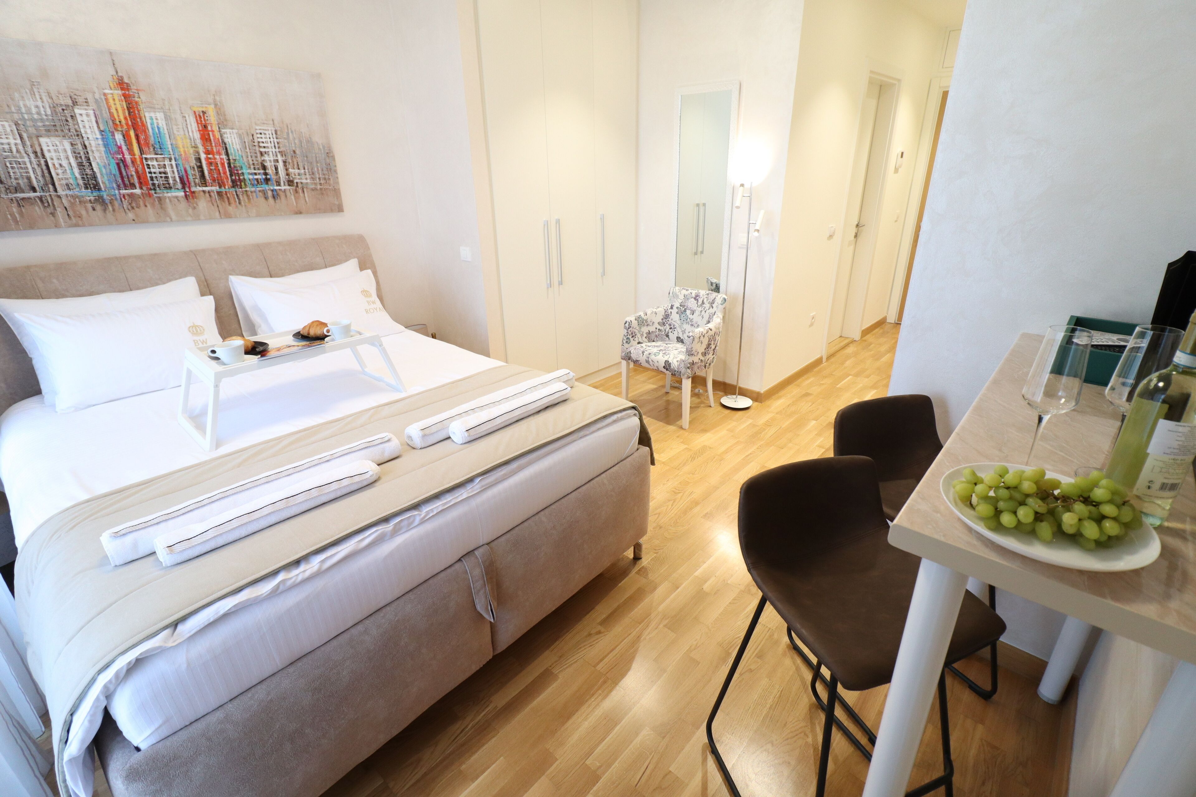 Une chambre d’hôtel avec un lit, une table à manger sur laquelle se trouve une assiette de raisins, une chaise et un miroir.