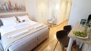 Une chambre d’hôtel avec un lit, une table à manger sur laquelle se trouve une assiette de raisins, une chaise et un miroir.