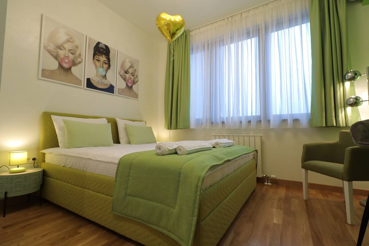 A hotel room with a bed, a chair, a nightstand, and a window with curtains.