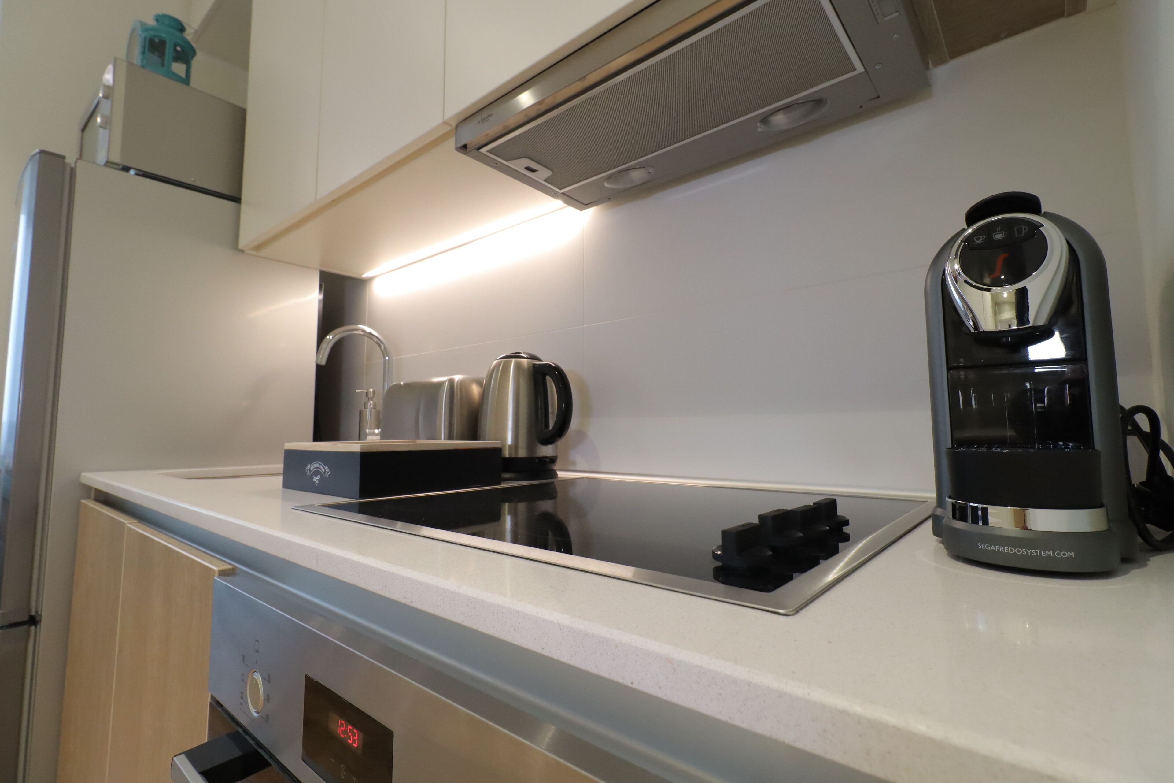 Ett modernt kök med en inbyggd ugn, en kaffebryggare och en vattenkokare på bänkskivan.