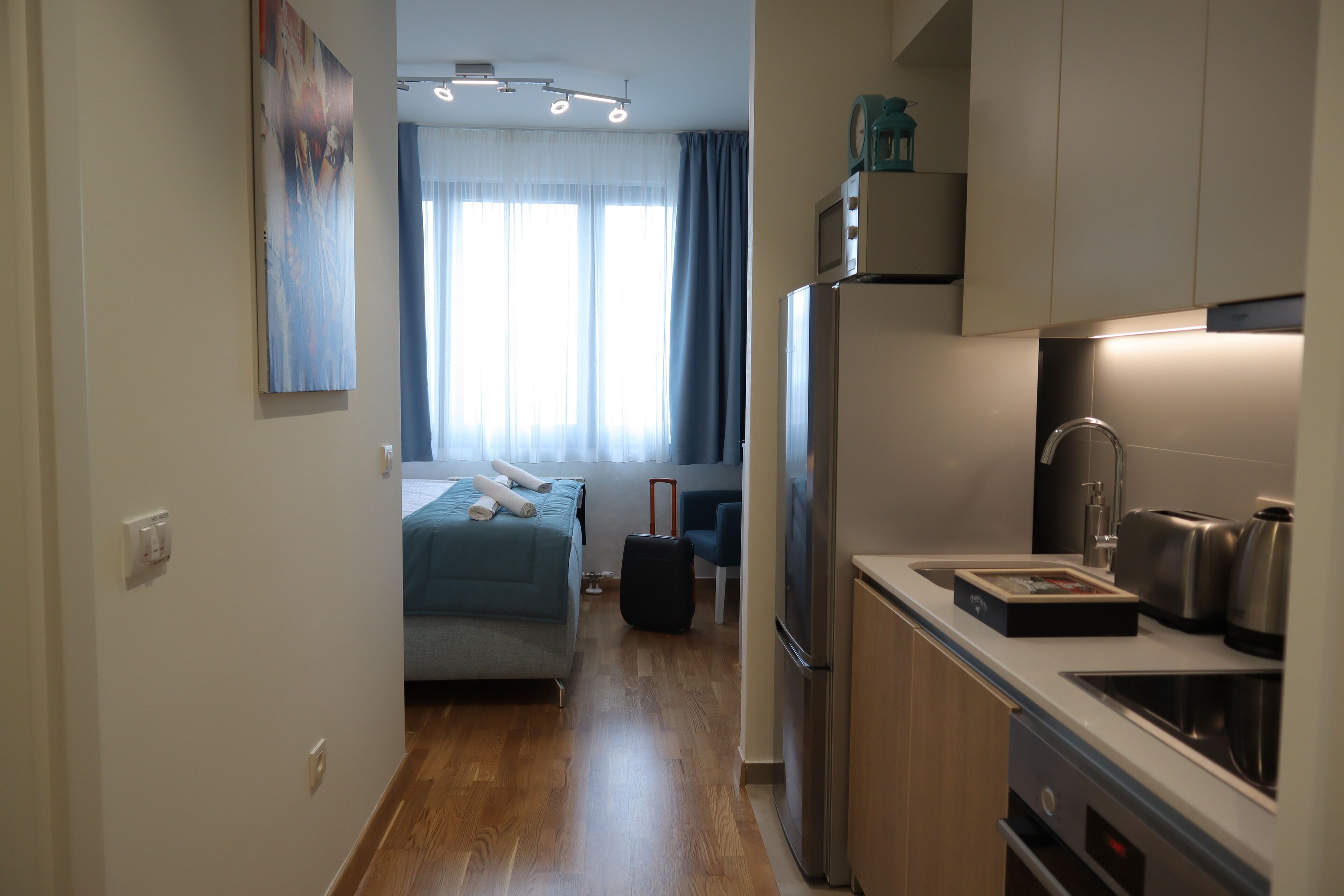 Quarto de hotel pequeno com cozinha compacta, uma cama e uma mala.