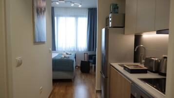 Quarto de hotel pequeno com cozinha compacta, uma cama e uma mala.