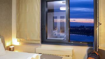 Una camera d'albergo con una grande finestra, un letto, un comodino e una valigia.