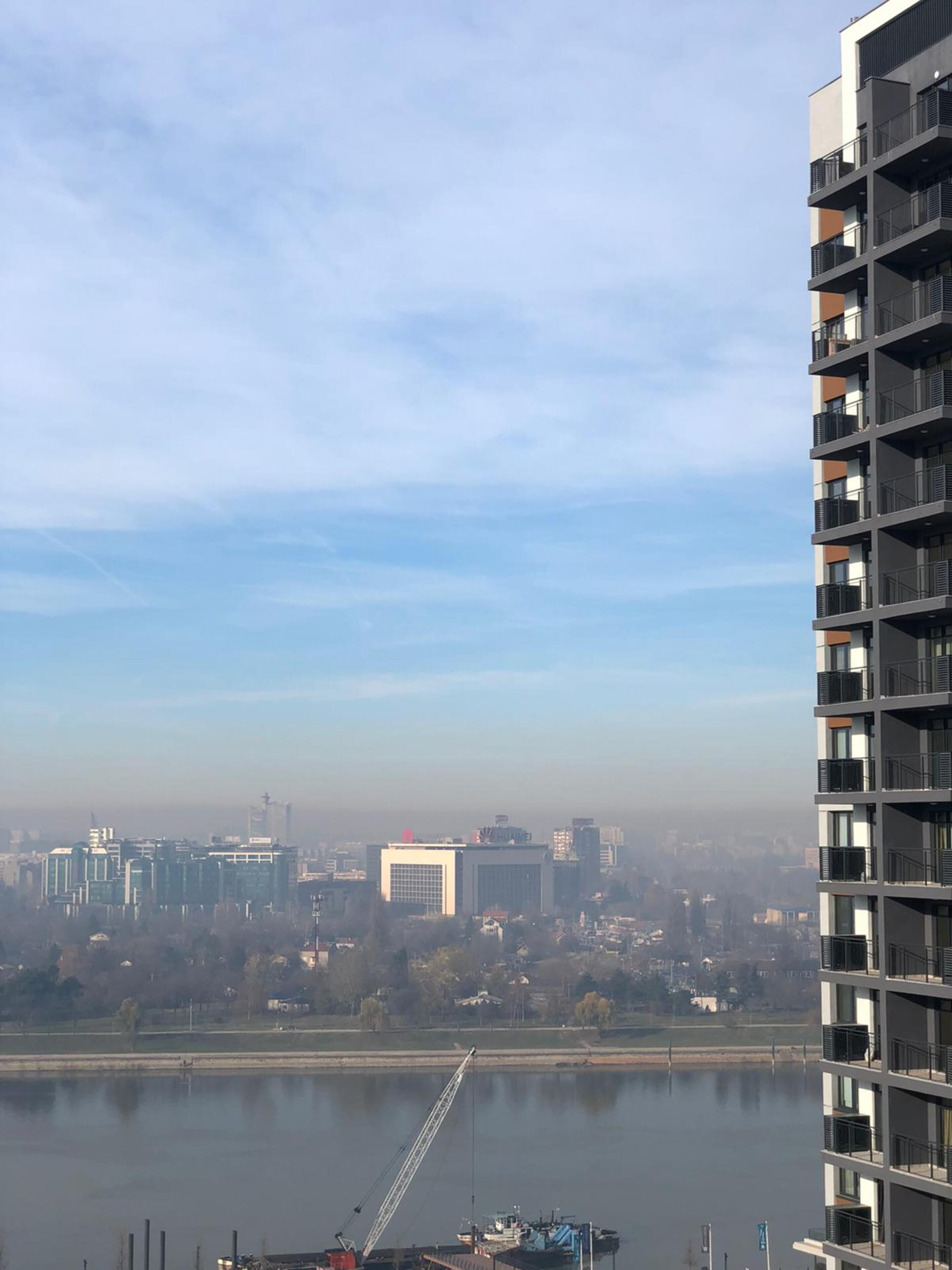 A high-rise building with multiple balconies overlooking a river and cityscape.