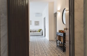 A hallway with patterned floor tiles, a white sofa with cushions, a wall-mounted mirror, and a small table with baskets.