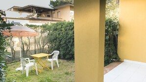 Eine Terrasse im Freien mit Tisch und Stühlen, umgeben von Grünpflanzen und einer gelben Wand.
