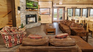 A cozy lodge interior with a stone fireplace, a large flat-screen TV, a sofa set, and wooden furniture.
