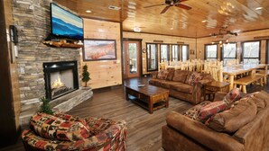 A cozy lodge interior with a stone fireplace, wooden furniture, and large windows.