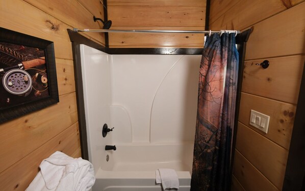 Une salle de bain rustique, avec des murs en bois, une douche, une serviette sur le sol et un tableau encadré au mur.