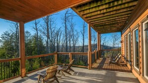 A wooden deck with chairs and a table, overlooking a forested area.