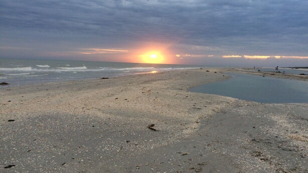 Ein Strand bei Sonnenuntergang, ruhiges Meer und einige Personen in der Ferne.