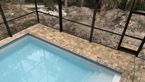 Ein Schwimmbecken mit gefliestem Sonnendeck, umgeben von einem Metallzaun.
