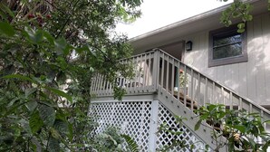 Ein Wohnhaus mit einer Holztreppe, die zu einem Balkon führt, umgeben von dichtem Grün.