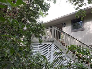 Staircase leads to a balcony with a lattice structure and a small window above, surrounded by lush greenery.