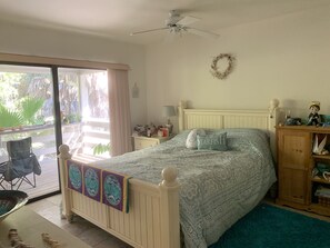 A bedroom with a bed, a nightstand, a chair, a wooden cabinet, and a view of the outdoors.
