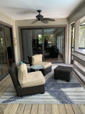 Relax in this stylish room with a large sliding door leading to a balcony, a dark wicker sofa, and a ceiling fan for ventilation.