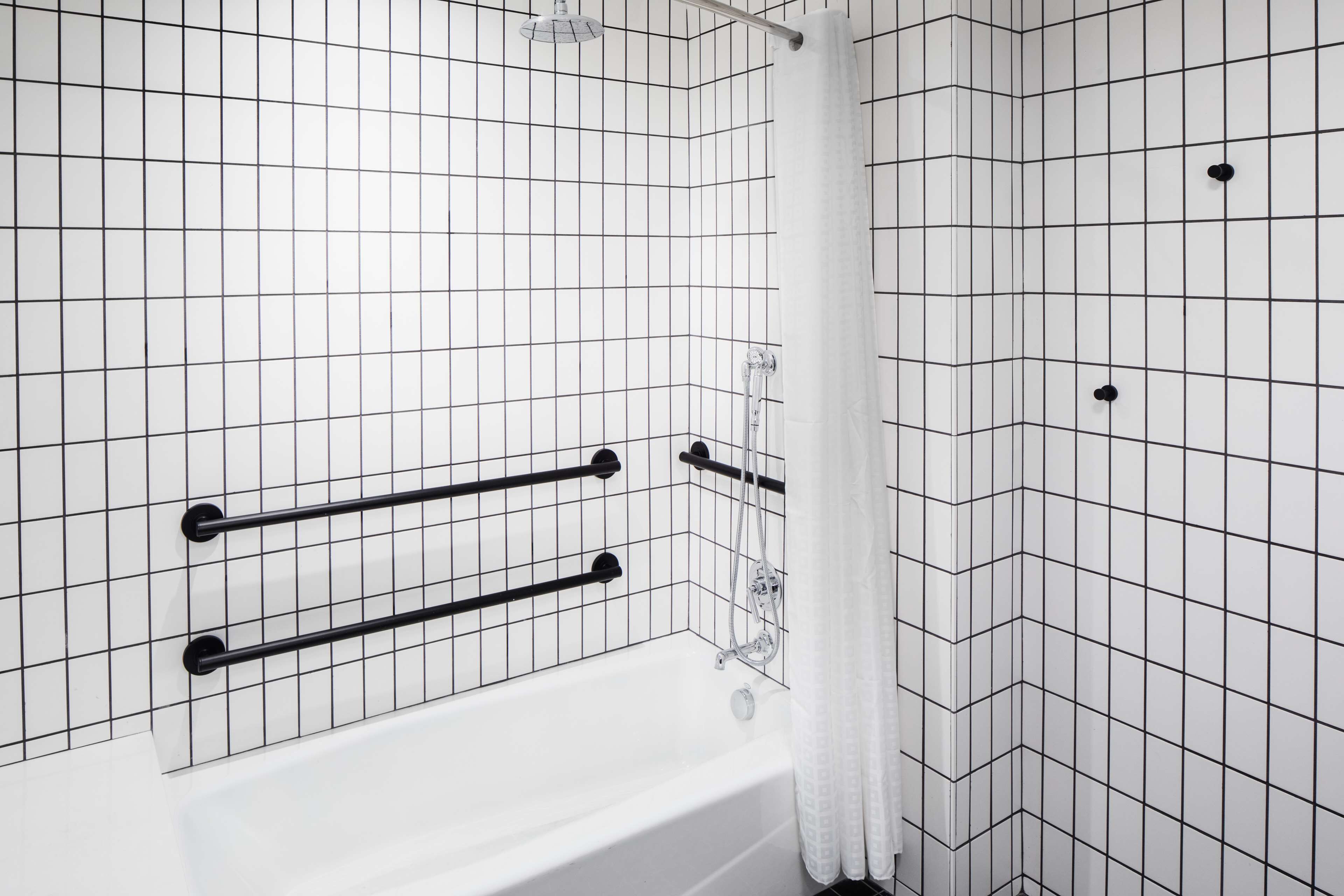 A bathroom with white tiled walls, a white bathtub, and black towel racks.