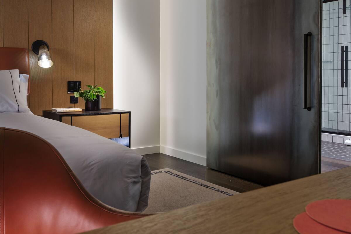 A modern bedroom with a wooden ceiling, a large sliding door, a bedside table with a lamp, and a bed with a red headboard.