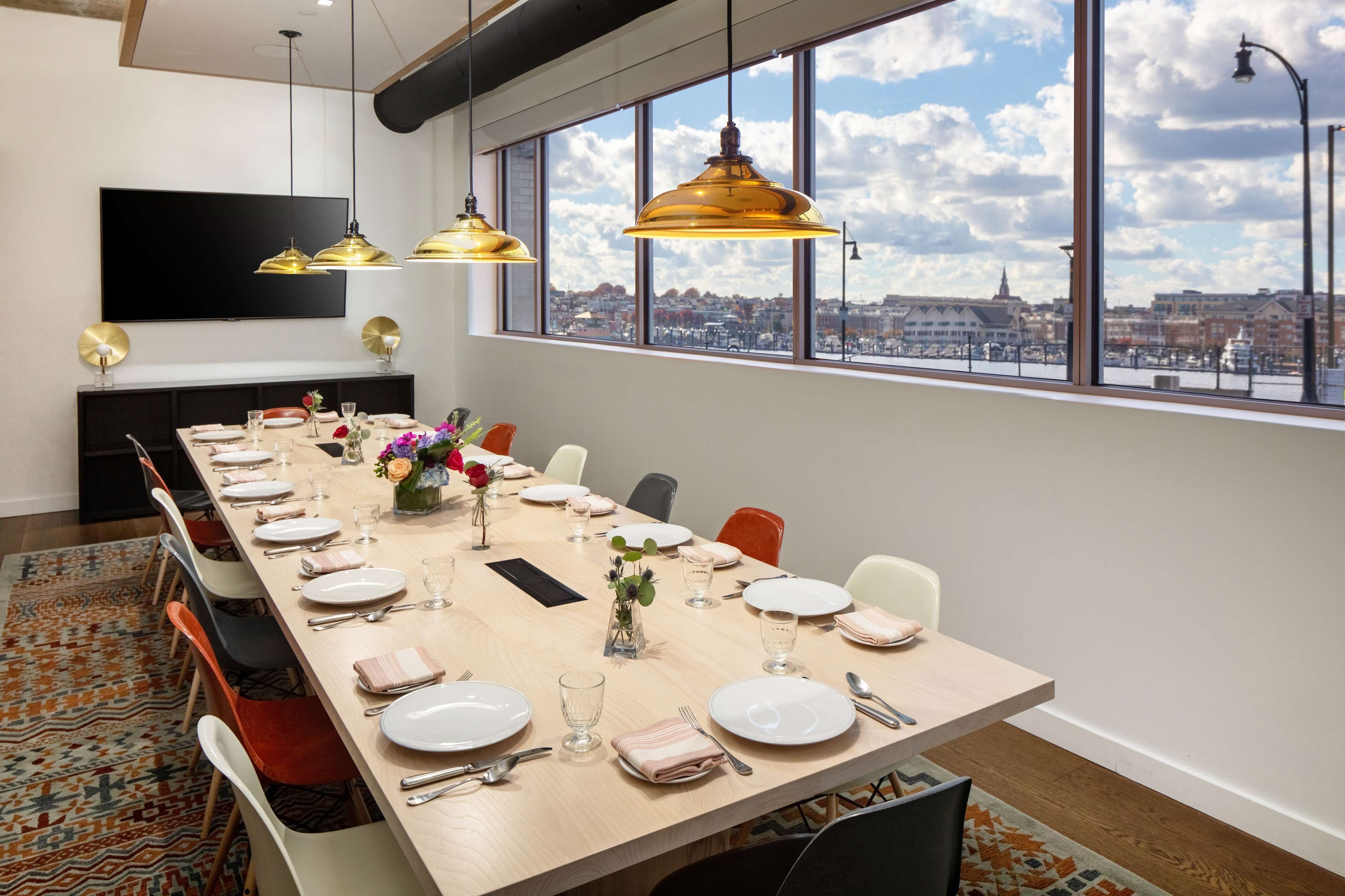 A long dining table set for a meal with a city view through large windows.
