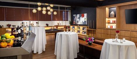 Un área de bar moderna con mesas redondas, una barra con botellas y un televisor montado en la pared.