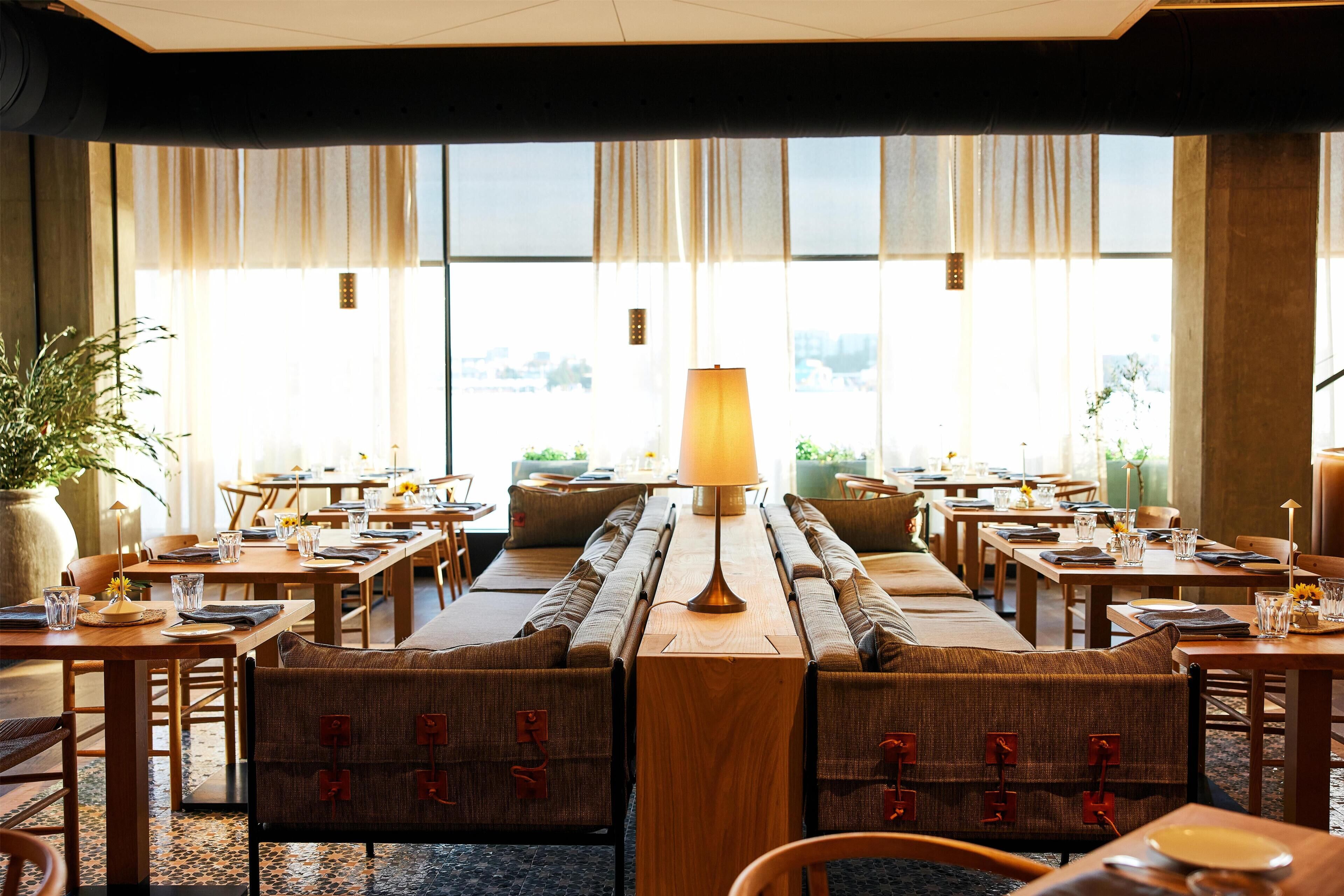 A restaurant with multiple tables and booths, large windows, and a central lamp.