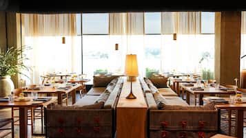 A restaurant with multiple tables and booths, large windows, and a central lamp.