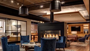 A modern lounge area with blue velvet armchairs, a central coffee table, and a fireplace. - Canopy by Hilton Baltimore Harbor Point (Baltimore)