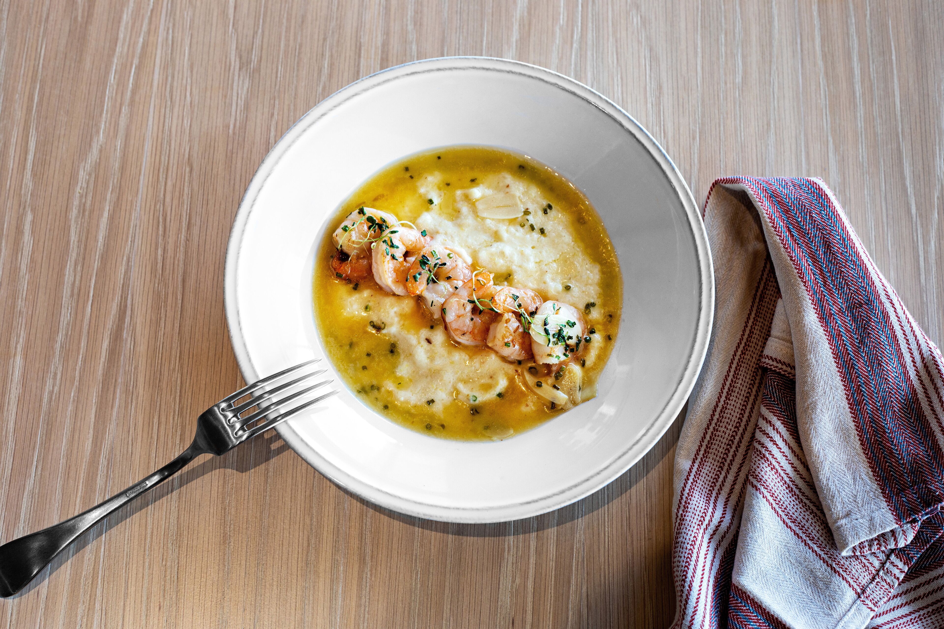 A bowl of soup with shrimp and herbs on a wooden table.