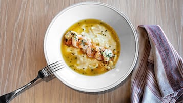 A bowl of soup with shrimp and herbs on a wooden table.