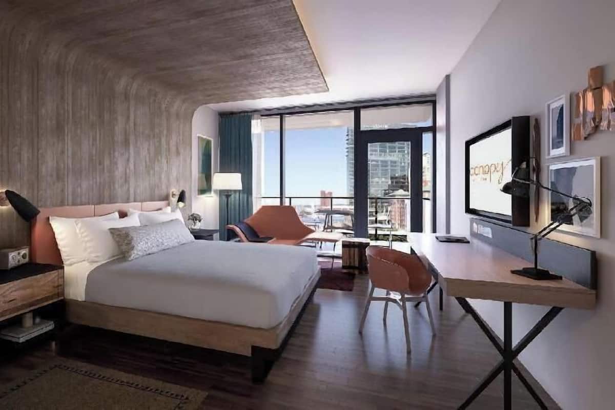 A modern hotel room with a large bed, a desk, a chair, and a balcony with a city view.