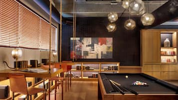 A modern lounge area with a pool table, bookshelves, and a large abstract painting on the wall.