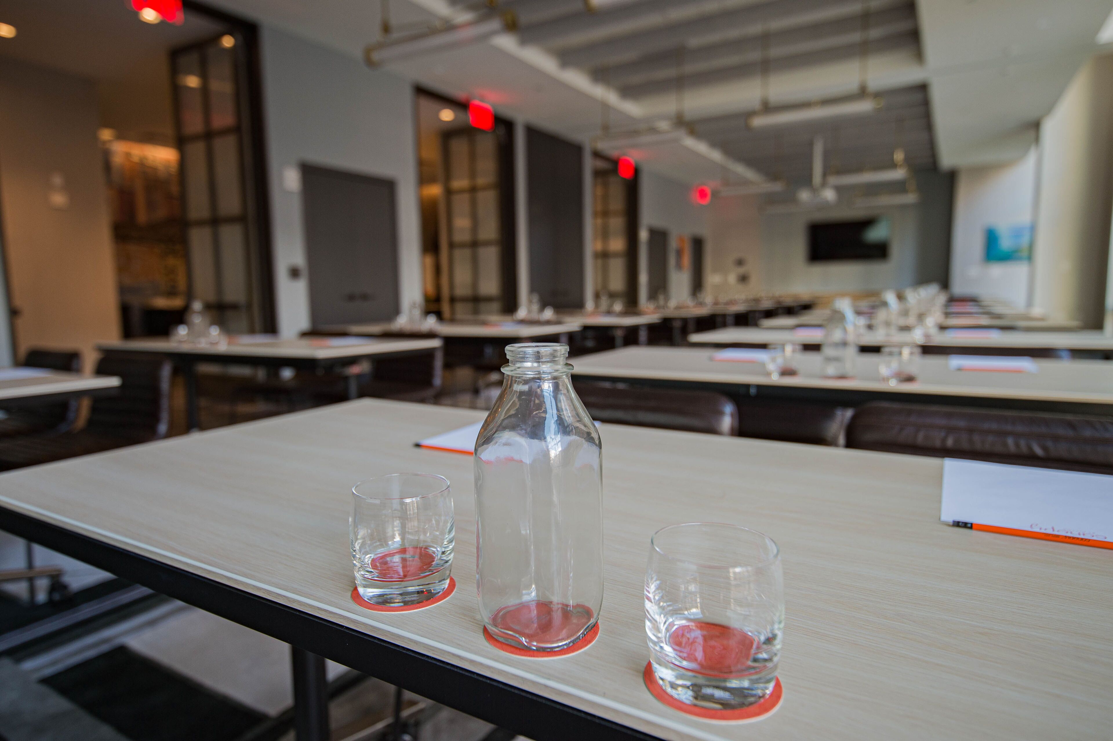 Un comedor moderno con mesas y sillas, una botella de vidrio transparente y dos vasos sobre una mesa.