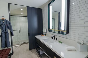A modern bathroom with a large mirror, two sinks, and a walk-in shower.