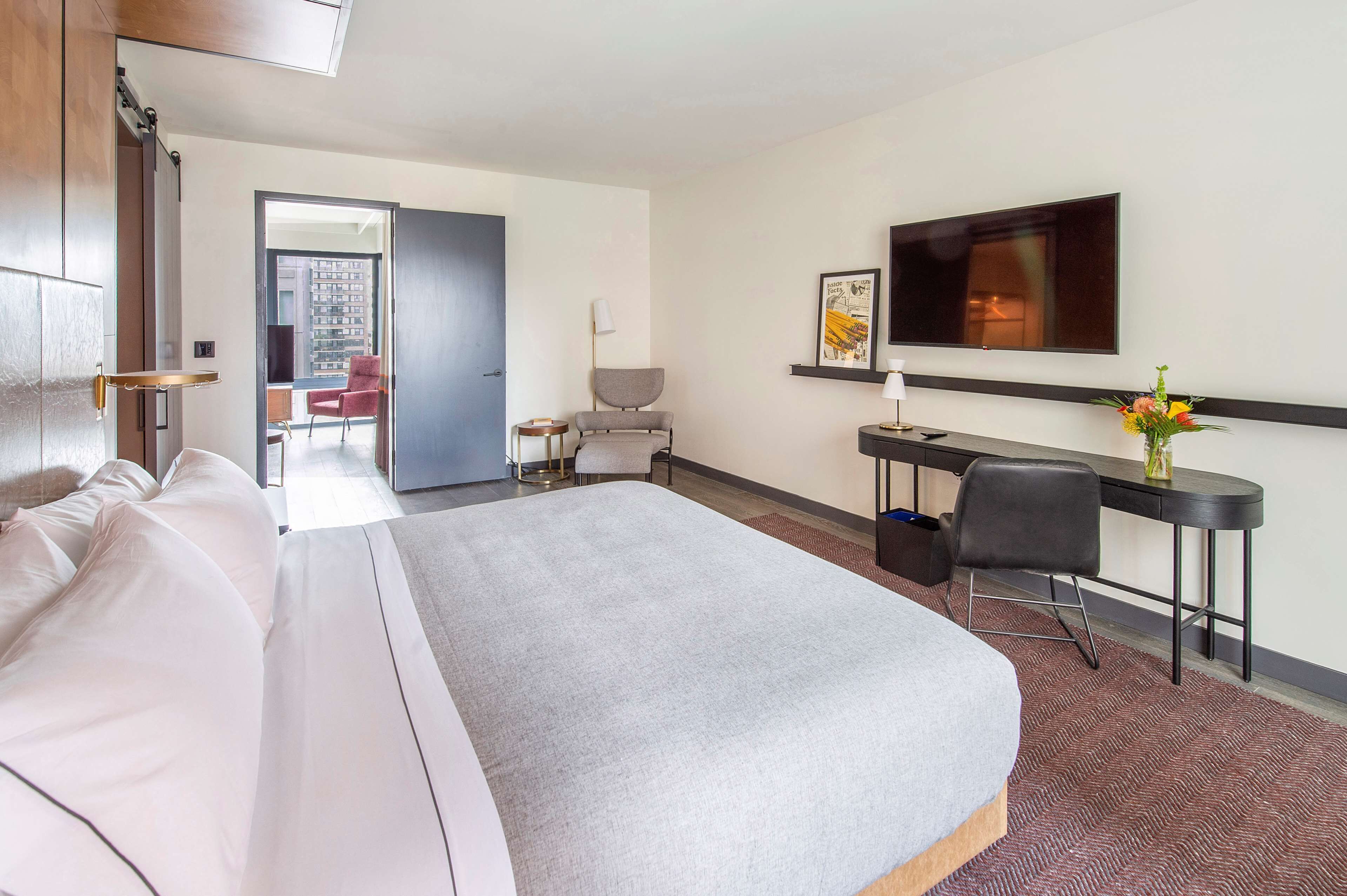Habitación de hotel con una cama grande, un escritorio, una silla, un televisor y vistas al exterior.