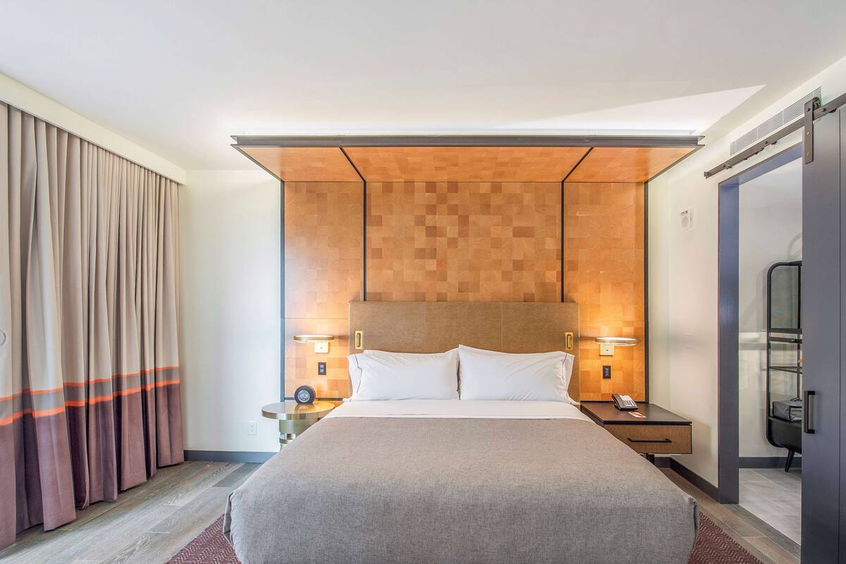 A hotel room with a large bed, wooden headboard, bedside tables with lamps, and a wardrobe.