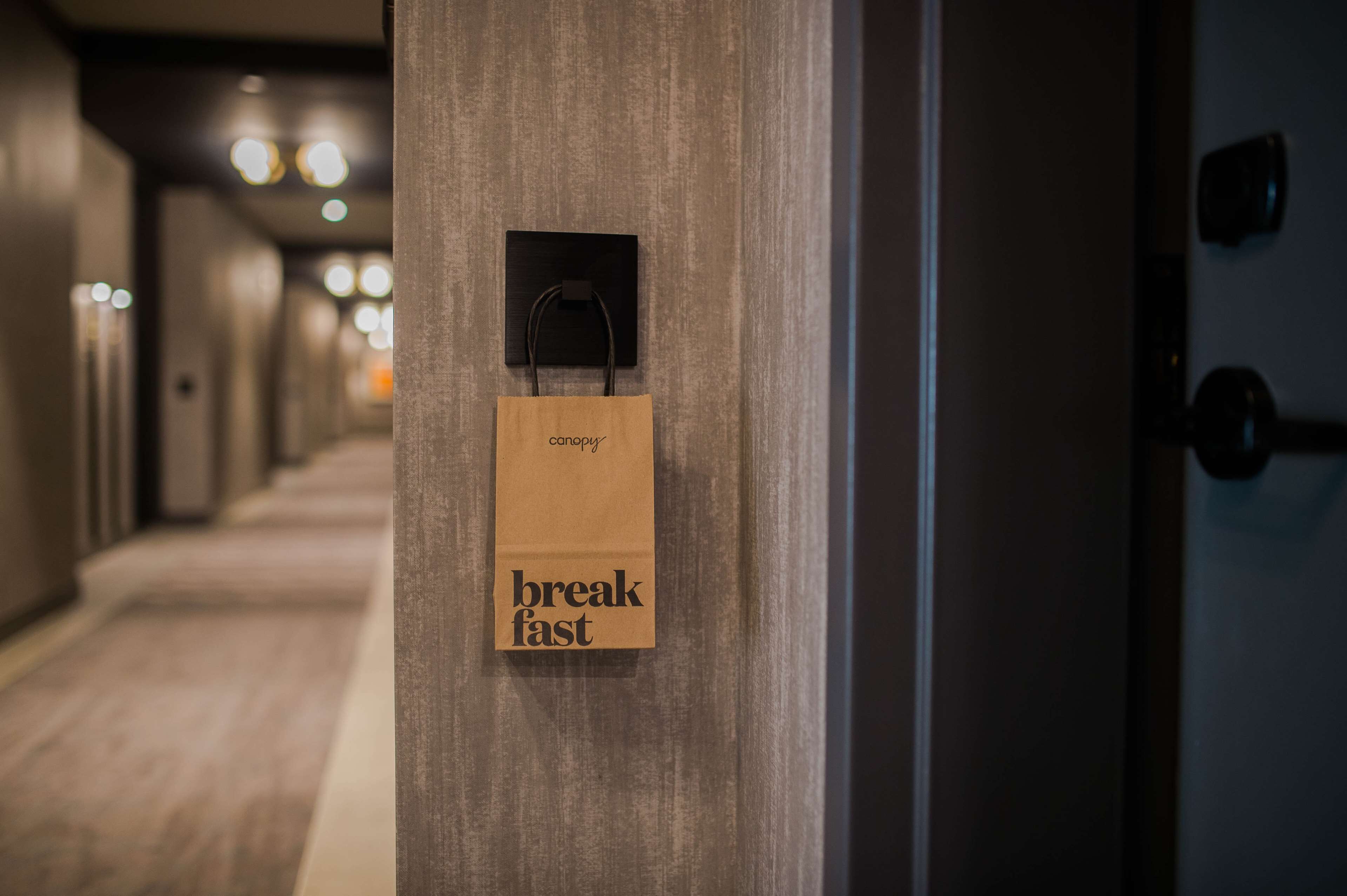 A hallway with a wooden door and a brown paper bag hanging on the door handle with the words "breakfast fast" on it.