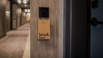 A hallway with a wooden door and a brown paper bag hanging on the door handle with the words "breakfast fast" on it.