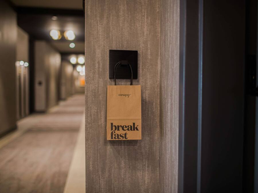 A hallway with a wooden door and a brown paper bag hanging on the door handle with the words "breakfast fast" on it.