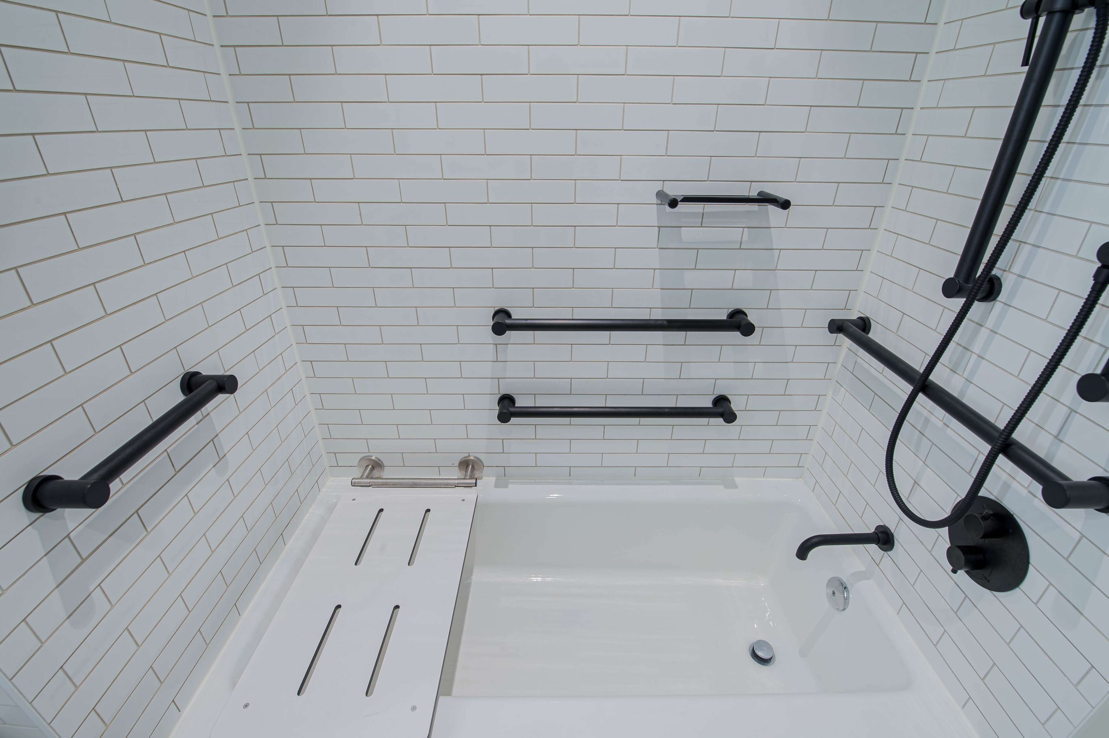 A bathroom with white tiled walls, a white bathtub, and black towel racks.