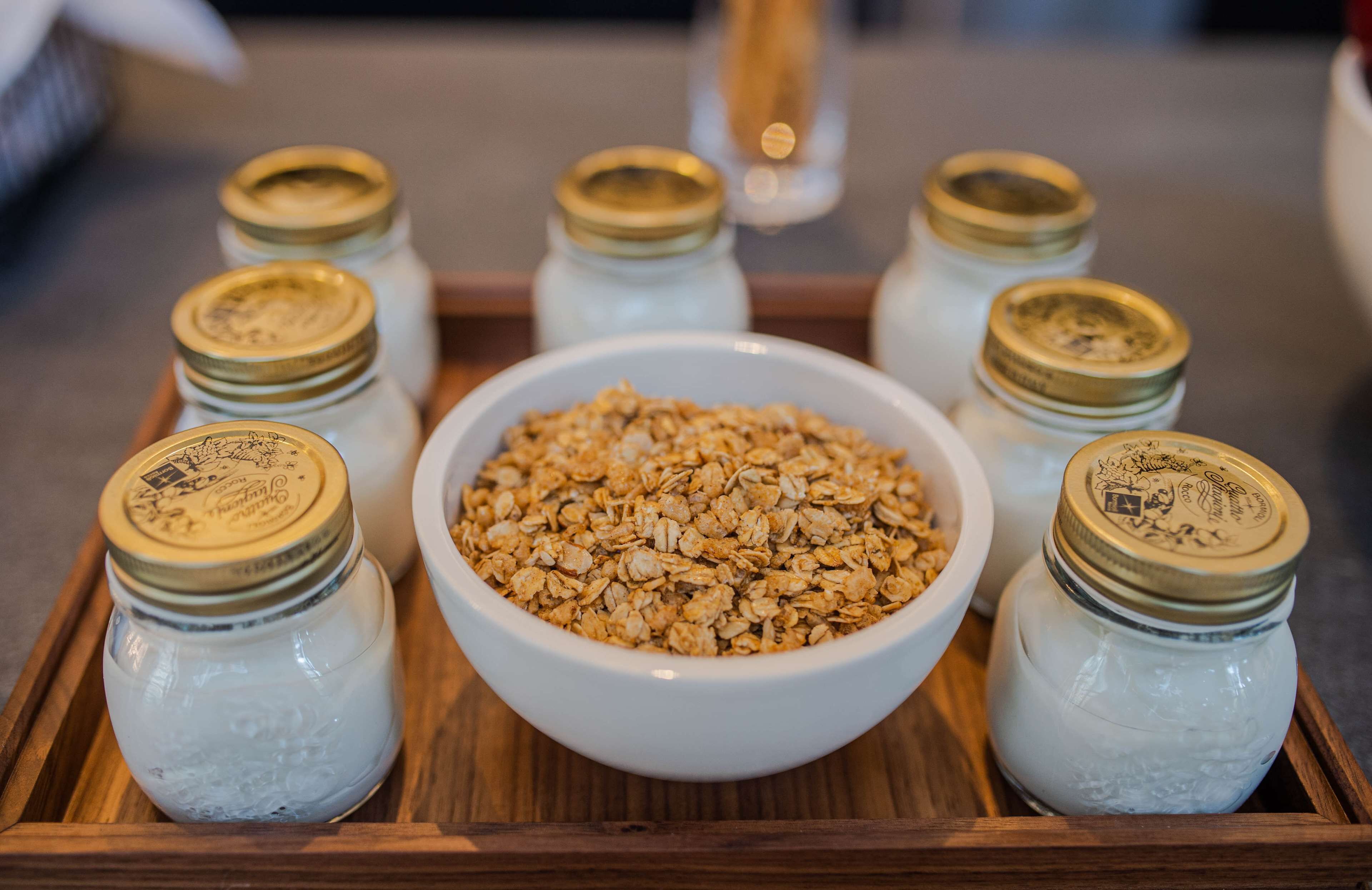 Una bandeja de madera con un tazón de granola en el centro, rodeado por seis frascos de vidrio con tapas metálicas.