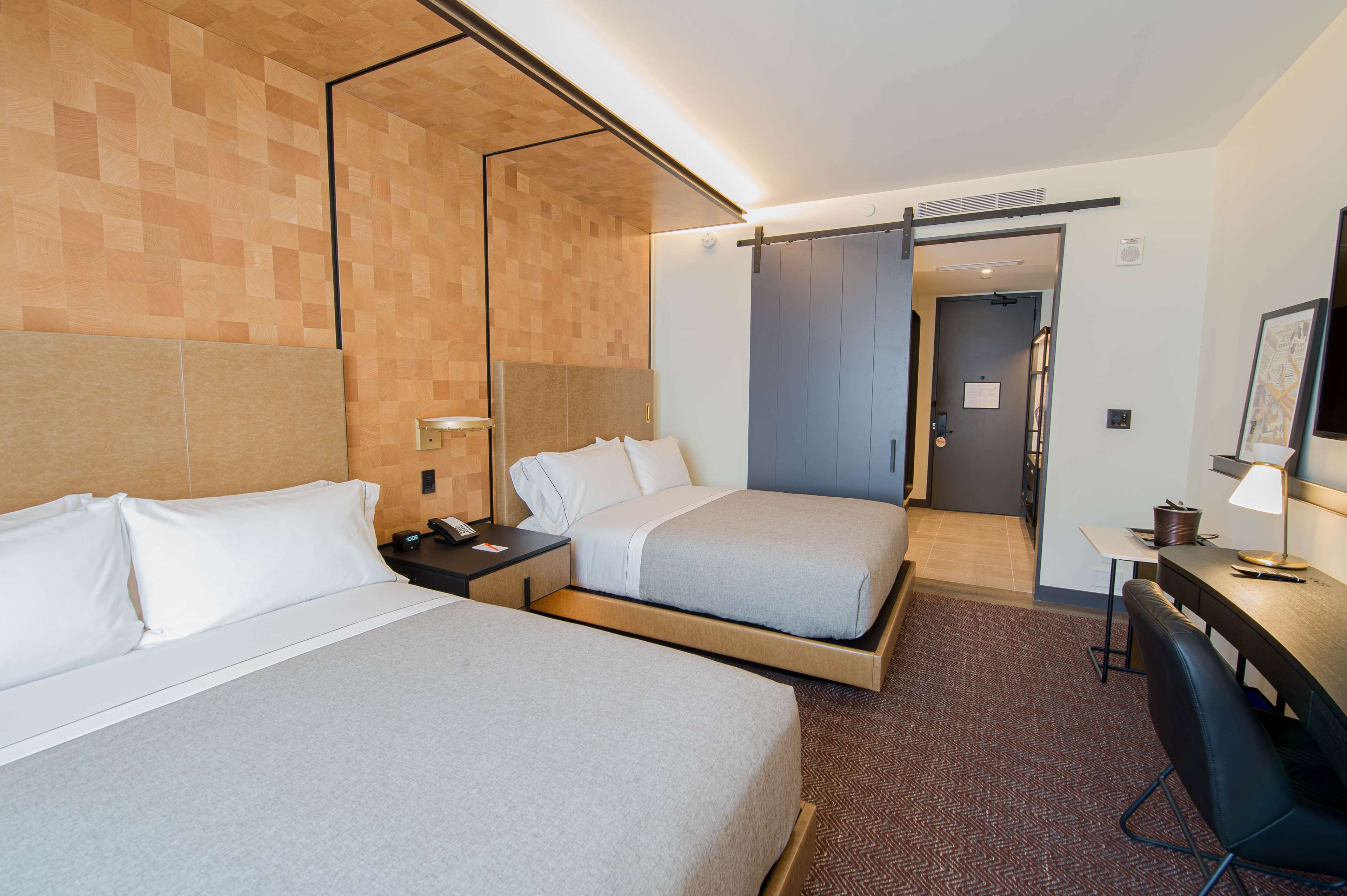 A hotel room with two beds, a desk, and a chair. There is a door leading to a bathroom and a hallway.