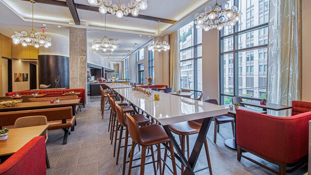 Ein moderner Essbereich mit langen Tischen, rot gepolsterten Stühlen und einem großen Fenster mit Blick auf die Stadt.