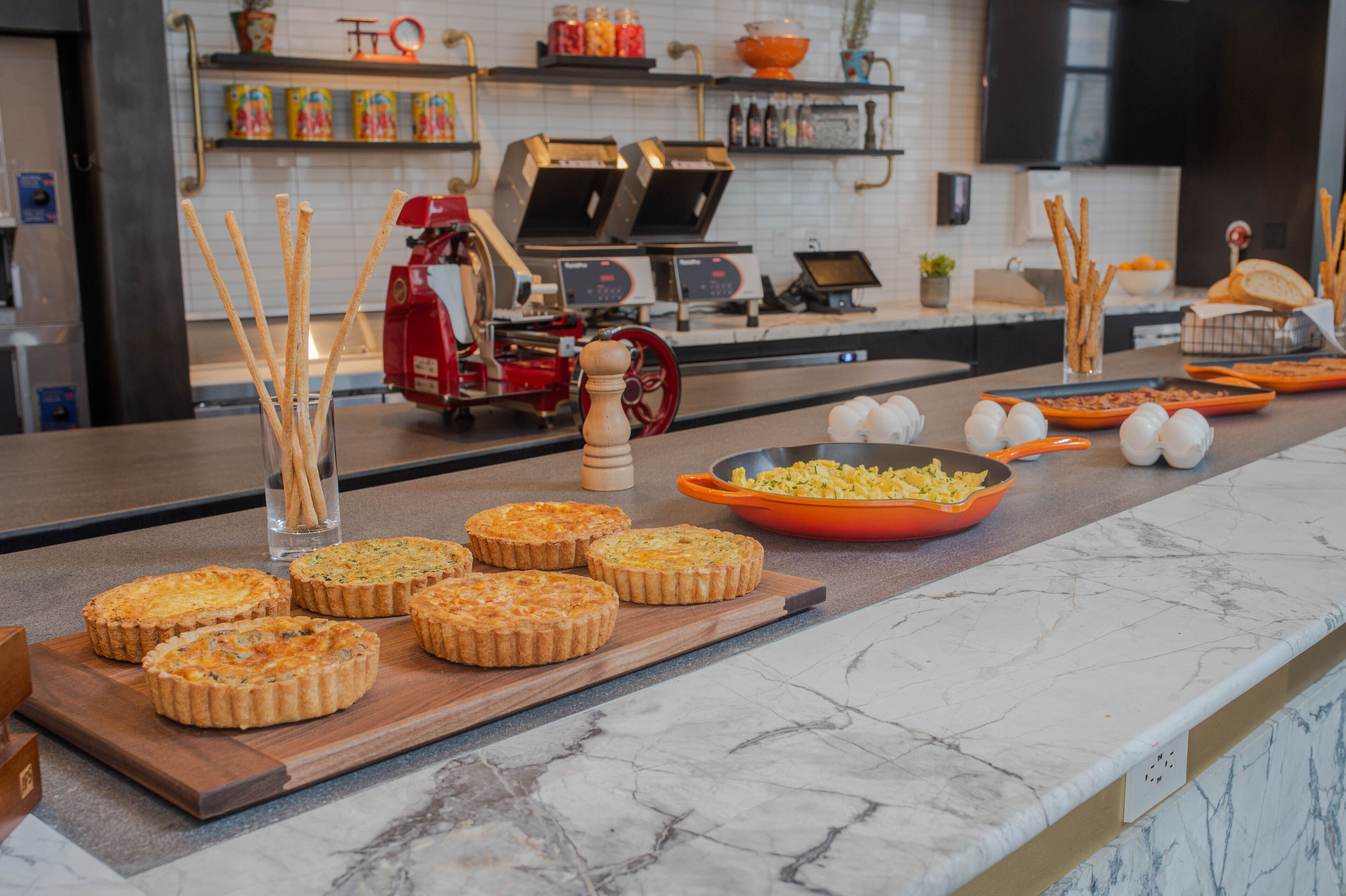 A kitchen counter with quiches, a grater, and a bowl of sliced vegetables.